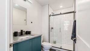 Un bagno moderno con doccia vetrata, un water bianco e un mobile lavabo verde acqua con specchio.