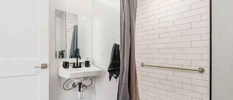 Une salle de bain avec un lavabo blanc, un miroir et une douche avec un rideau.