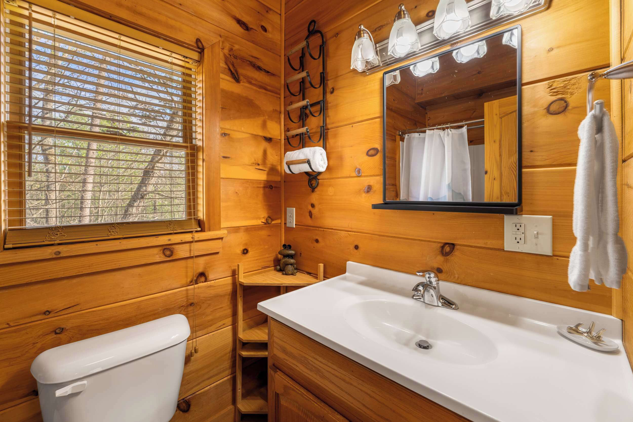 A wooden cabin bathroom with a toilet, sink, and mirror.