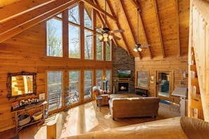 A log cabin interior with a fireplace, large windows, and a cozy seating area. - Smokies Getaway for 6 wPrivate Hot Tub & Mtn View (Sevierville)