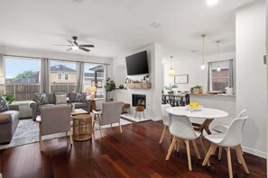 Ein modernes Wohnzimmer mit einer Sofagarnitur, einem Esstisch mit Stühlen, einem Kamin und einem an der Wand montierten Fernseher.