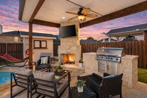 Eine Terrasse im Freien mit Kamin aus Stein, Grill und Gartenmöbeln.