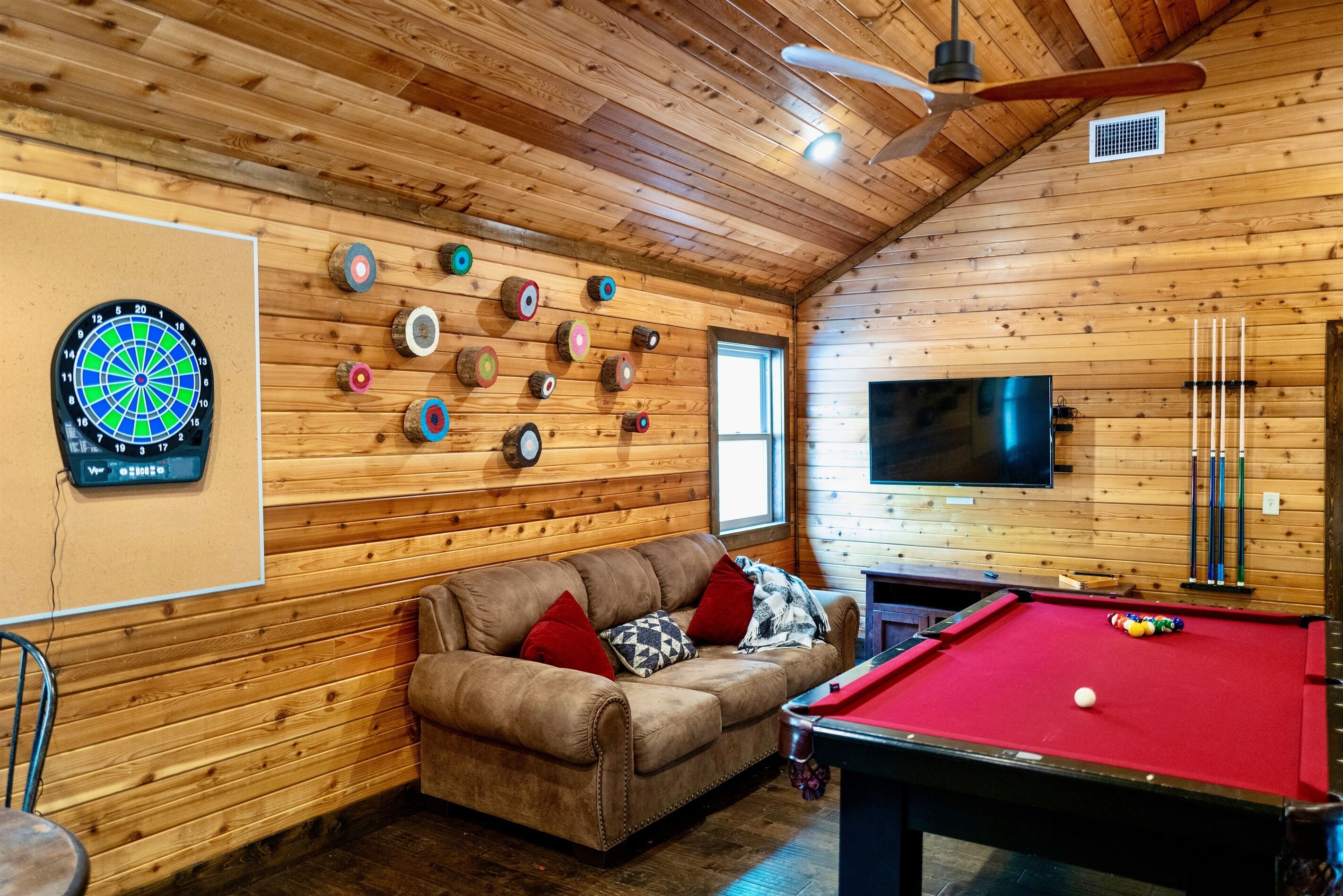 Een gezellige kamer met een pooltafel, een dartbord en een televisie.