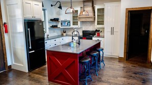 Une cuisine moderne avec des meubles blancs, un réfrigérateur noir, un îlot central rouge et des tabourets de bar.