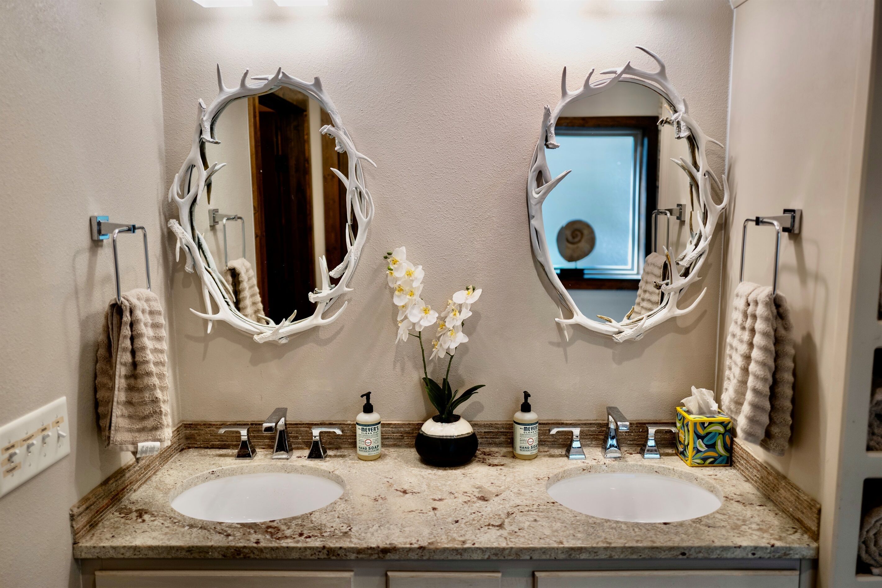 Een badkamer met twee wastafels, een spiegel en een vaas met bloemen.