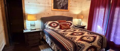 A wooden-paneled room with a bed, two bedside lamps, a chandelier, and a red curtain.