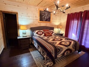 Ein Zimmer mit Holzwandverkleidung, einem Bett, zwei Nachttischlampen, einer Kristallleuchtre und einem roten Vorhang.