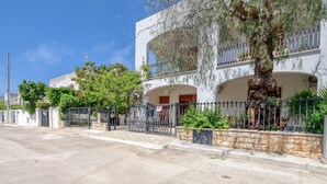 Un edificio residencial con fachada blanca, varios balcones y un árbol en primer plano.