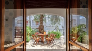 Un patio al aire libre con una mesa y sillas de madera, un árbol y vistas de un edificio con balcones.