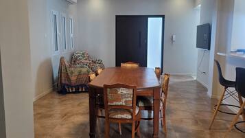 Un comedor con mesa y sillas de madera, un sofá estampado y una puerta que da a otra habitación.
