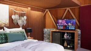 A bedroom with a bed, a TV on a wooden stand, a wall-mounted decoration, and a stone wall.