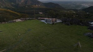 A grassy outdoor area with a small building, surrounded by hills and a distant view of a valley.