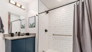Un bagno moderno con doccia, un mobile lavabo con specchio e un porta asciugamani.