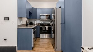 Una cucina compatta con mobili blu, un forno a microonde, un fornello e un frigorifero.