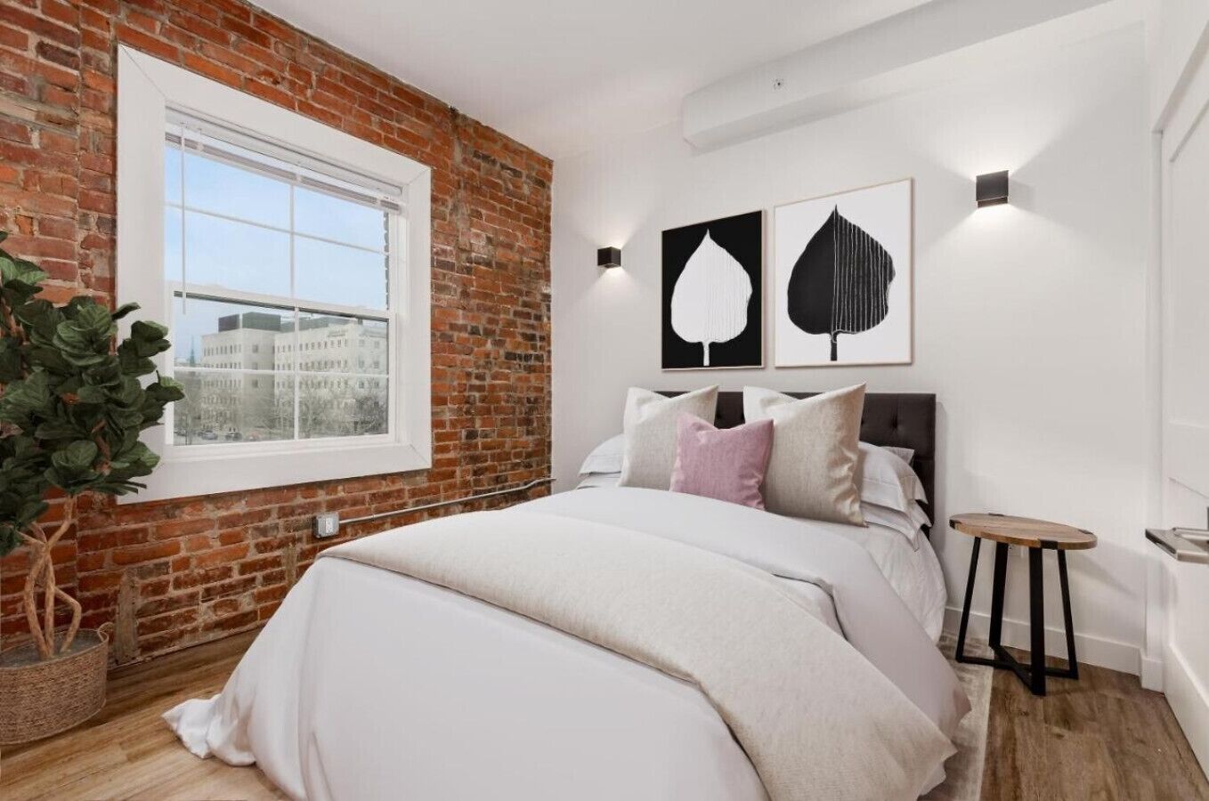 Ein Schlafzimmer mit Backsteinwand, einem großen Fenster, einem Bett mit Kissen und zwei Wandleuchten.