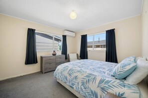 A bedroom with a bed, dresser, chair, and a window with curtains.