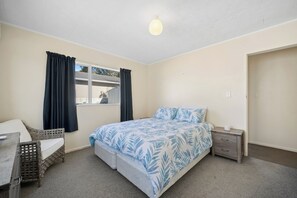 Un dormitorio con cama, mesita de noche, silla y ventana con cortinas.