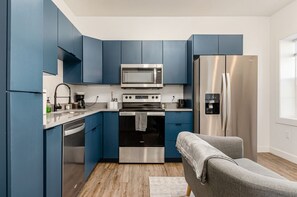 A modern kitchen with blue cabinets, stainless steel appliances, and a grey sofa. - Pet-Friendly Downtown Studio w/ Pool Table (Columbus)