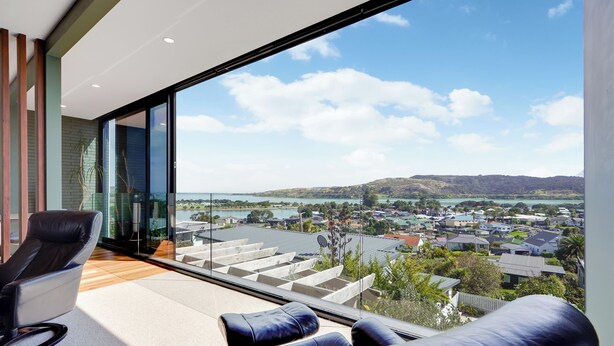 A modern room with a large glass window, a black leather sofa, and a wooden floor.