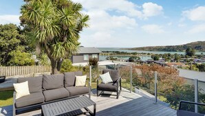 A deck with a sofa and armchair, overlooking a lake and houses.