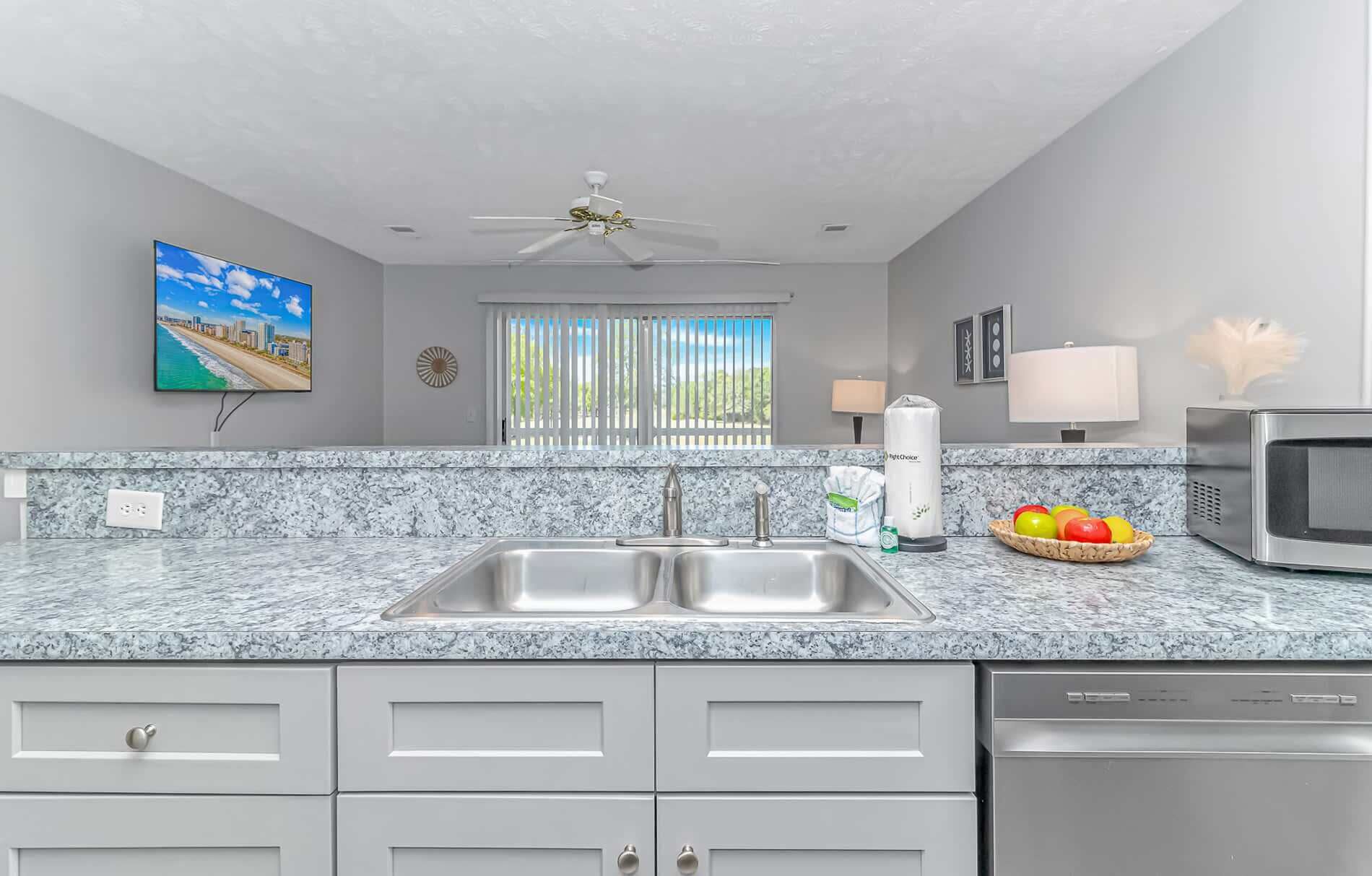 Una cocina con encimeras de granito, electrodomésticos de acero inoxidable, ventilador de techo y una ventana con persianas.