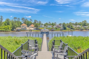A wooden dock leading to a gazebo with chairs, overlooking a calm lake with houses and greenery in the background. - Waterway Village 12E (Myrtle Beach)