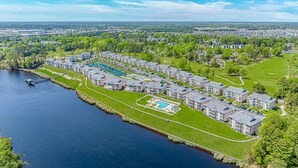 Een wooncomplex met meerdere appartementencomplexen, een centraal gelegen zwembad en een steiger die in het water uitloopt.