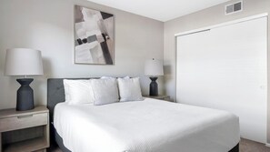 A hotel room with a bed, two bedside tables with lamps, a large abstract painting on the wall, and a closed door. - Landing | Modern 2BD, Gym, Pool (Vestavia Hills)