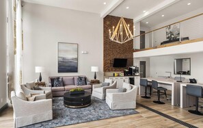 A modern living room with a sofa, coffee table, and a dining area with a kitchen in the background. - Landing | Modern 2BD, Gym, Pool (Vestavia Hills)