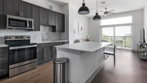 A modern kitchen with stainless steel appliances, a large island, and a balcony with a view. - Landing | Spectacular 1BD, Pool, Gym (Austin)
