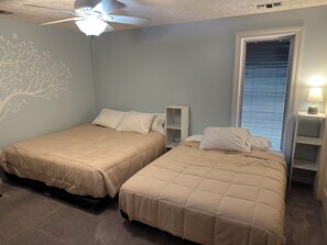 Ein Schlafzimmer mit zwei Betten, einem Deckenventilator, einem Fenster mit Jalousien und einem Wandregal mit einer Lampe.