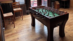 Une pièce avec un baby-foot, des chaises en bois, une table et une vue par la fenêtre.