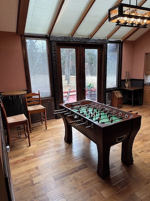 Ein Zimmer mit einem Kicker, Holzstühlen, einem Tisch und Blick durch ein Fenster.