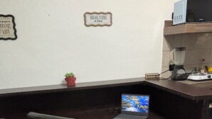 Ein kleiner Büroraum mit Schreibtisch, Stuhl und einem Laptop. An der Wand hängt ein Schild und auf dem Schreibtisch steht eine kleine Pflanze.