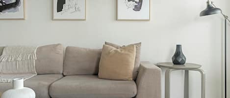 A modern living room with a beige sofa, a small side table with a vase, and abstract art on the wall.