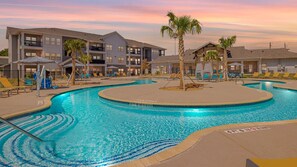 A swimming pool with a 4 ft depth marker, surrounded by lounge chairs and palm trees, with multi-story buildings in the background. - Landing | Modern 1BD, Pool, Clubhouse (Pflugerville)