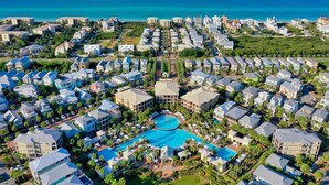 Vista aérea de un complejo turístico con varias edificaciones, una piscina central y una costa en el fondo.