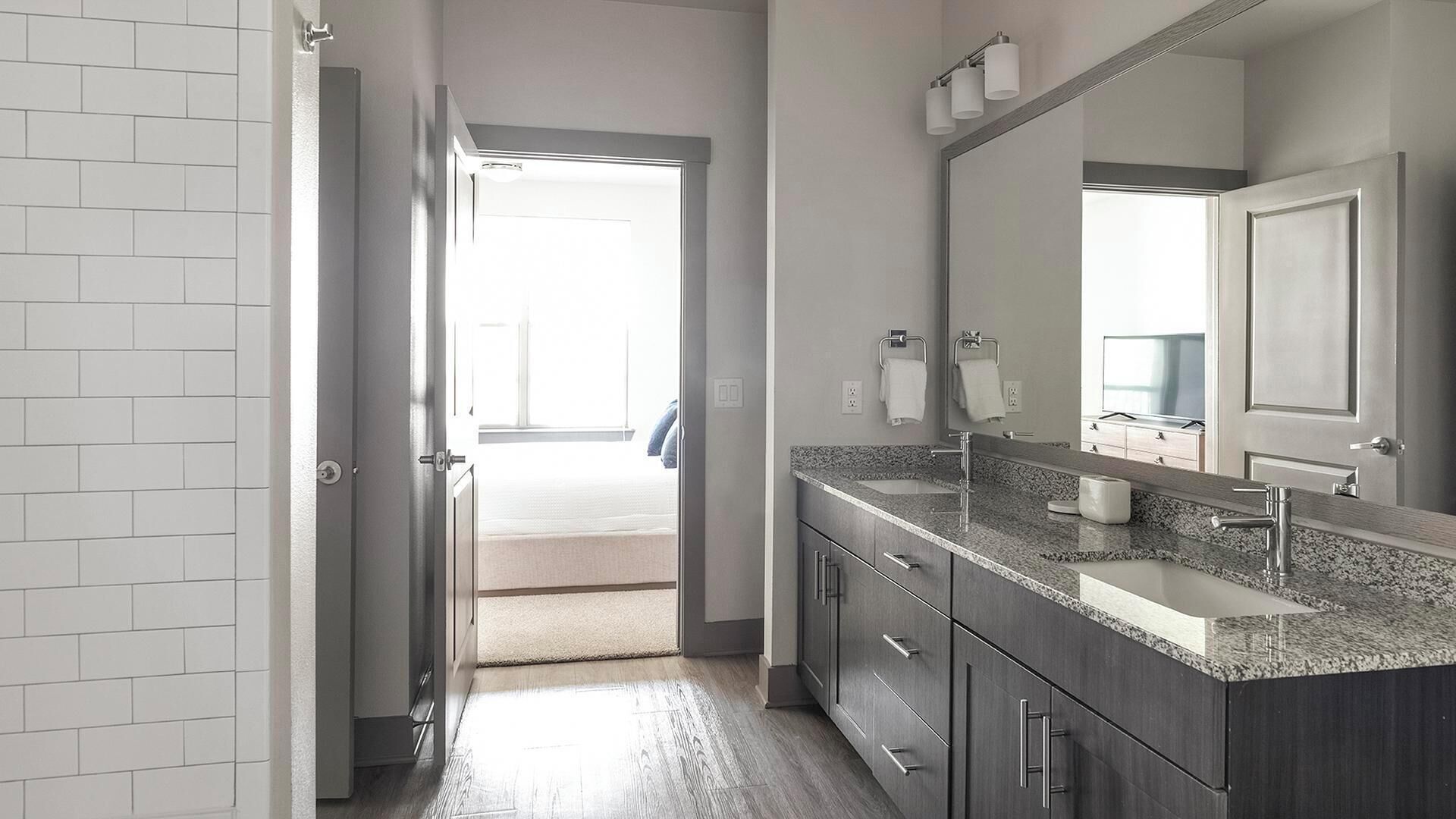 A modern bathroom with a granite countertop, a large mirror, and a walk-in shower.