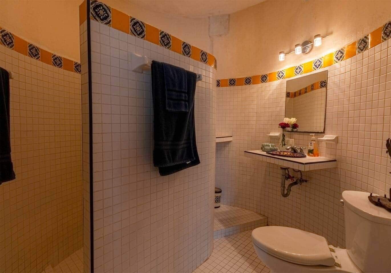 Un baño con inodoro, lavamanos y zona de ducha, con piso y paredes cubiertas de azulejos y un borde decorativo.