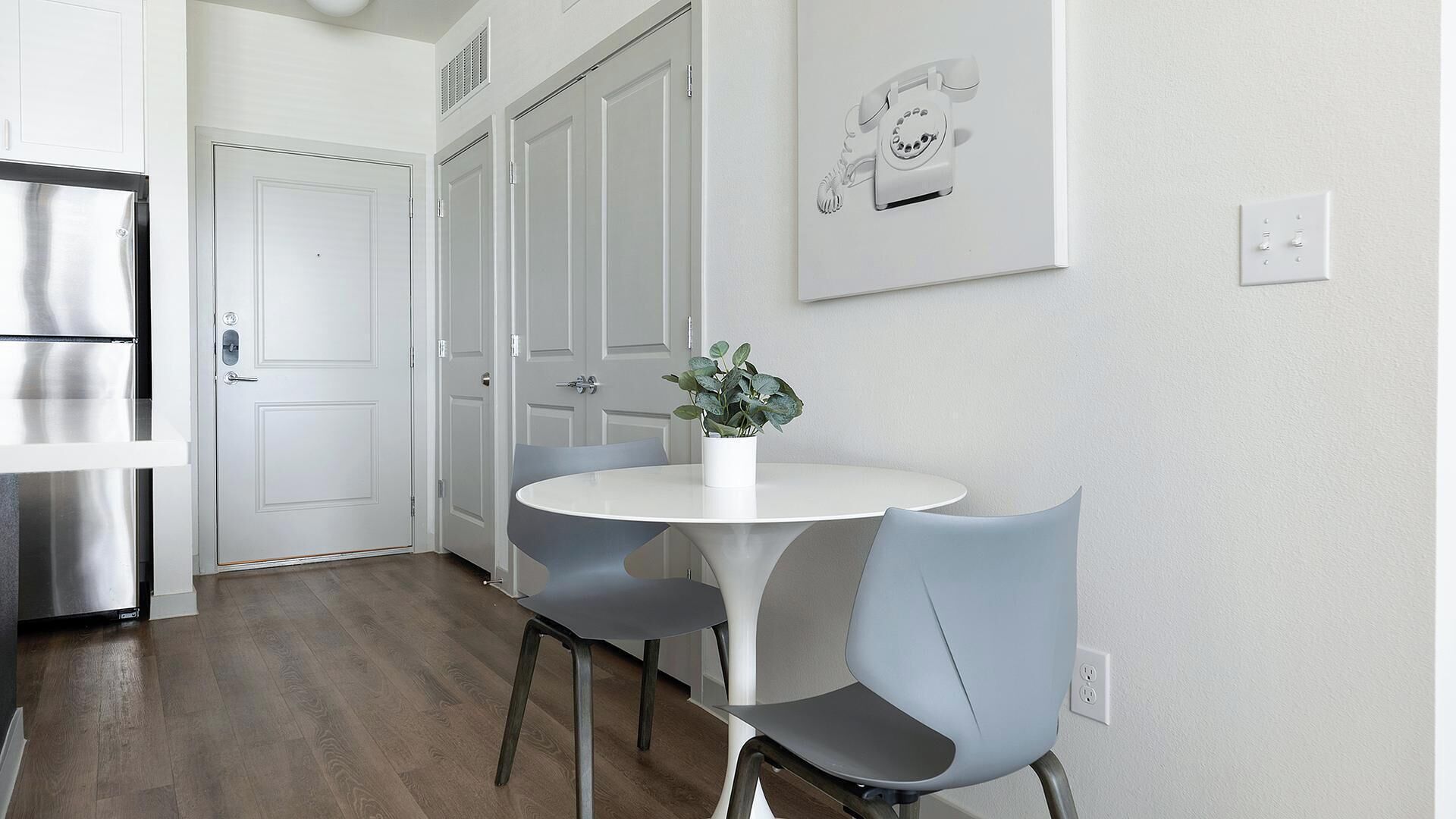 A modern kitchen with a stainless steel refrigerator, white cabinets, and a round dining table with two chairs.