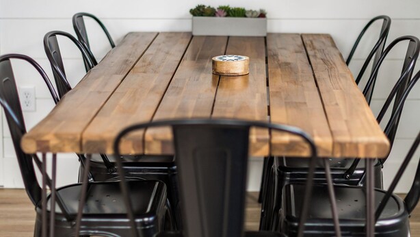 Uma mesa de jantar de madeira com cadeiras pretas, uma janela acima e uma pequena planta no parapeito.