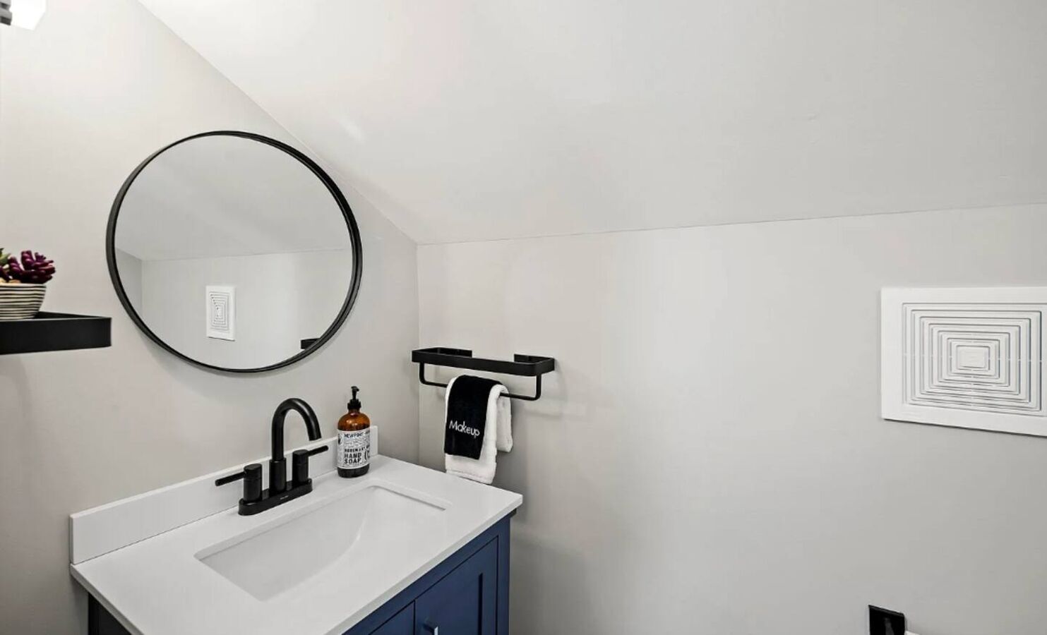 Un baño moderno con un lavamanos blanco, un grifo negro y un espejo redondo.