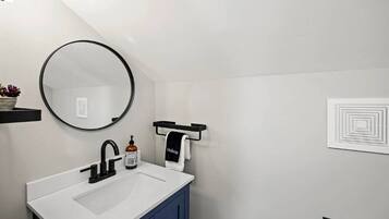 Un baño moderno con un lavamanos blanco, un grifo negro y un espejo redondo.