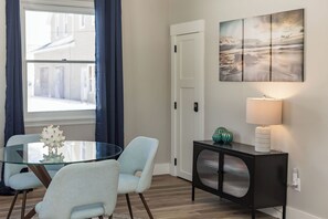 A dining area with a glass table, two chairs, a black console, and a wall-mounted lamp.