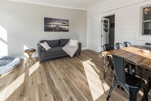 A modern living room with a grey sofa, wooden dining table, and chairs.