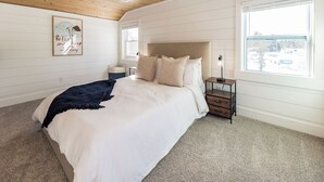 Quarto com cama grande, mesa de cabeceira, abajur, janela e luminária no teto.