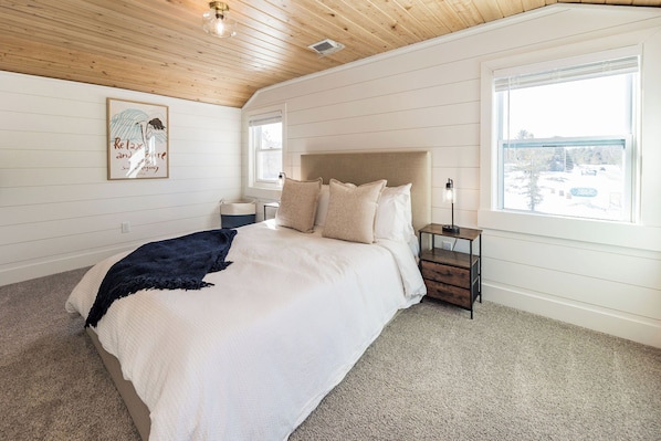 A bedroom with a large bed, a nightstand, a bedside lamp, a window, and a ceiling light fixture.