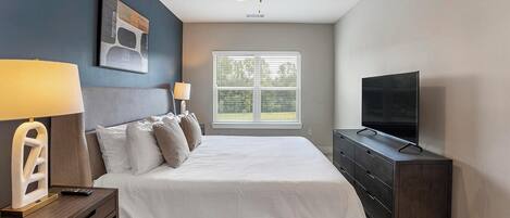 A bedroom with a bed, a TV, a desk with a lamp, and a ceiling fan.