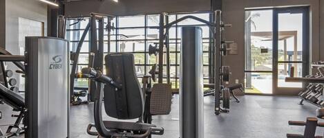 Un gimnasio con equipos de ejercicio variados, ventanas amplias y un letrero de salida.
