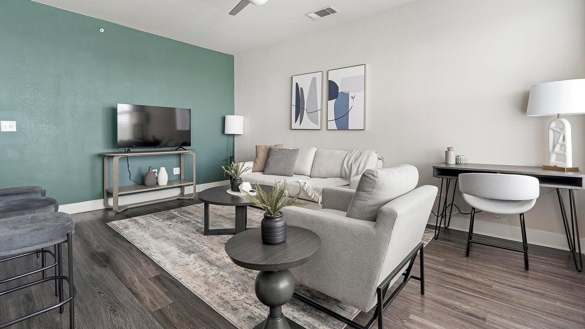 A modern living room with a sofa, coffee table, TV, and a desk with a lamp.